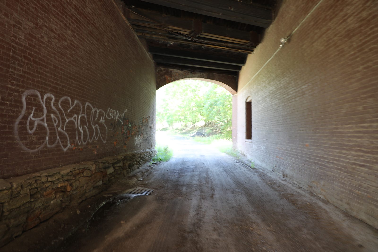 Brick underpass with graffiti, leading out to a gravel road